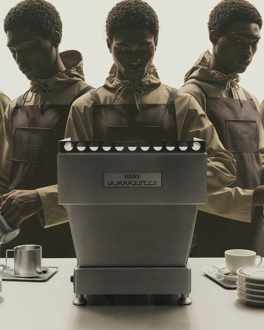 Baristas con el delantal de Rains y La Marzocco junto a una Linea Mini con placa de Rains