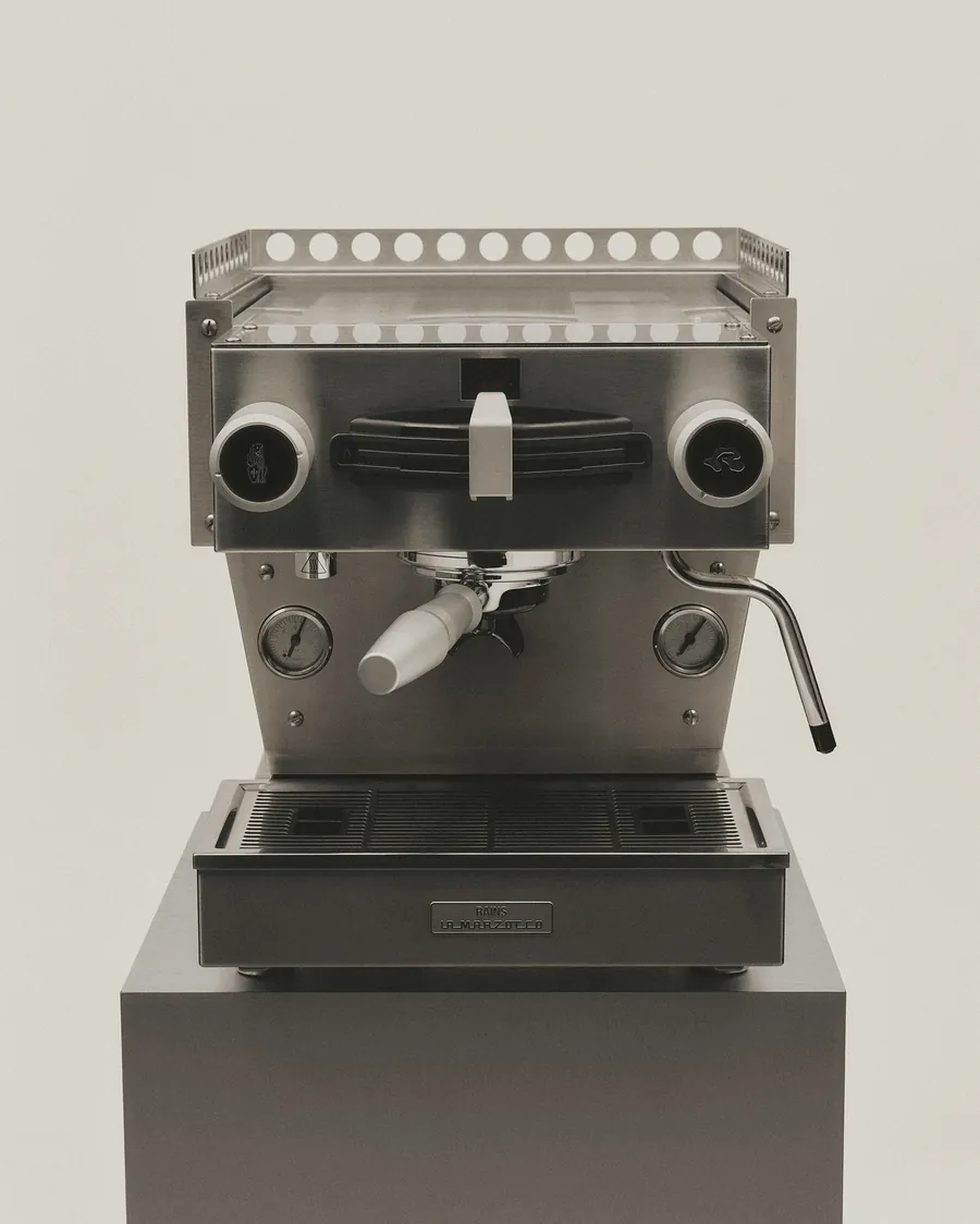 Linea Mini de Officine Fratelli Bambi de la colaboración entre La Marzocco y Rains, con placa de Rains, sobre un pedestal